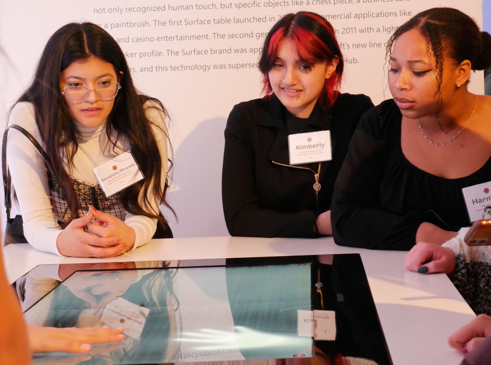 Three young women look down at a screen. 