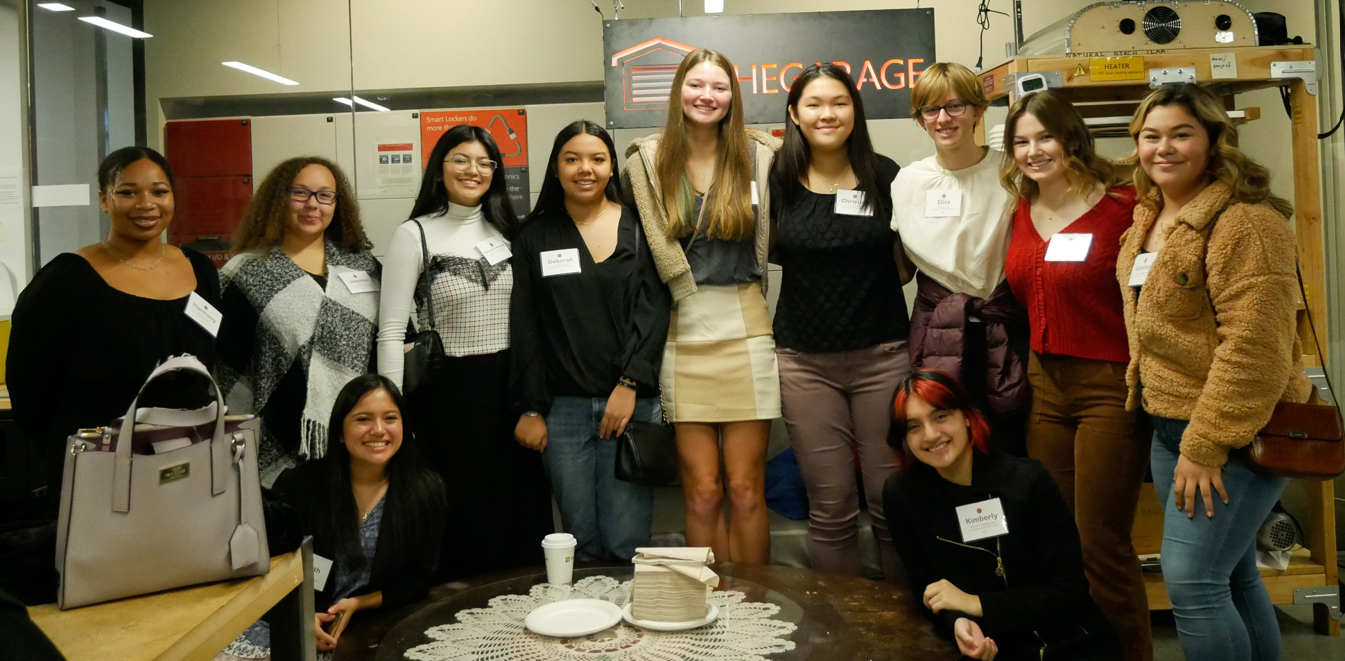 A group of young women stand in a makerspace and smile