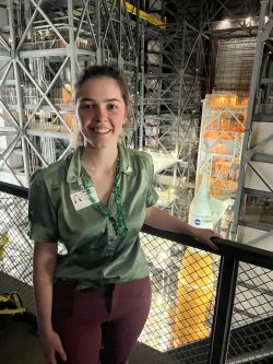 girl stands on platform in front of a rocket