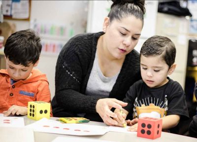 Frau und zwei kleine Kinder sitzen am Tisch und zeichnen