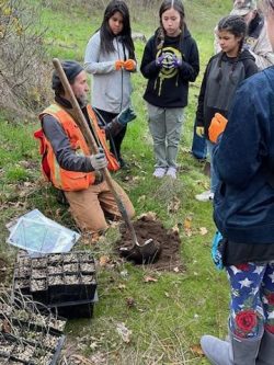 outdoor educator instructs students while digging a hole