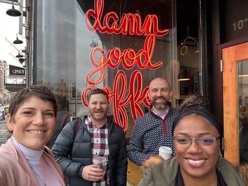 Four people smile in selfie in front of coffee shop