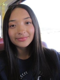 Young woman with brown hair and brown eyes smiles at the camera