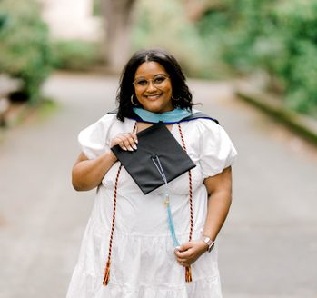 Woman in a white dress and graduation stole holds a graduation cap.